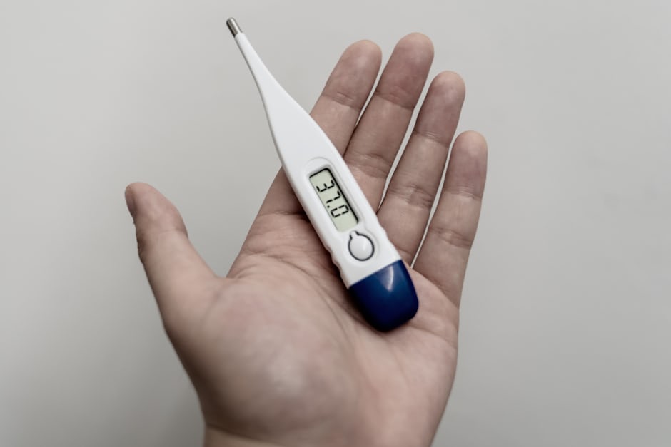 A person checking their temperature with a thermometer, a possible warning sign of infection