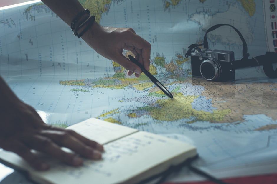 A traveller planning a trip on a map with a notebook and camera